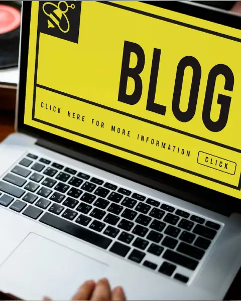 A laptop displaying a bright yellow blog interface with the text "CLICK HERE FOR MORE INFORMATION" prominently featured.