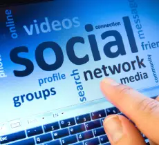 A finger tapping a touch screen displaying a social media word cloud with words like "social network," "videos," and "groups."